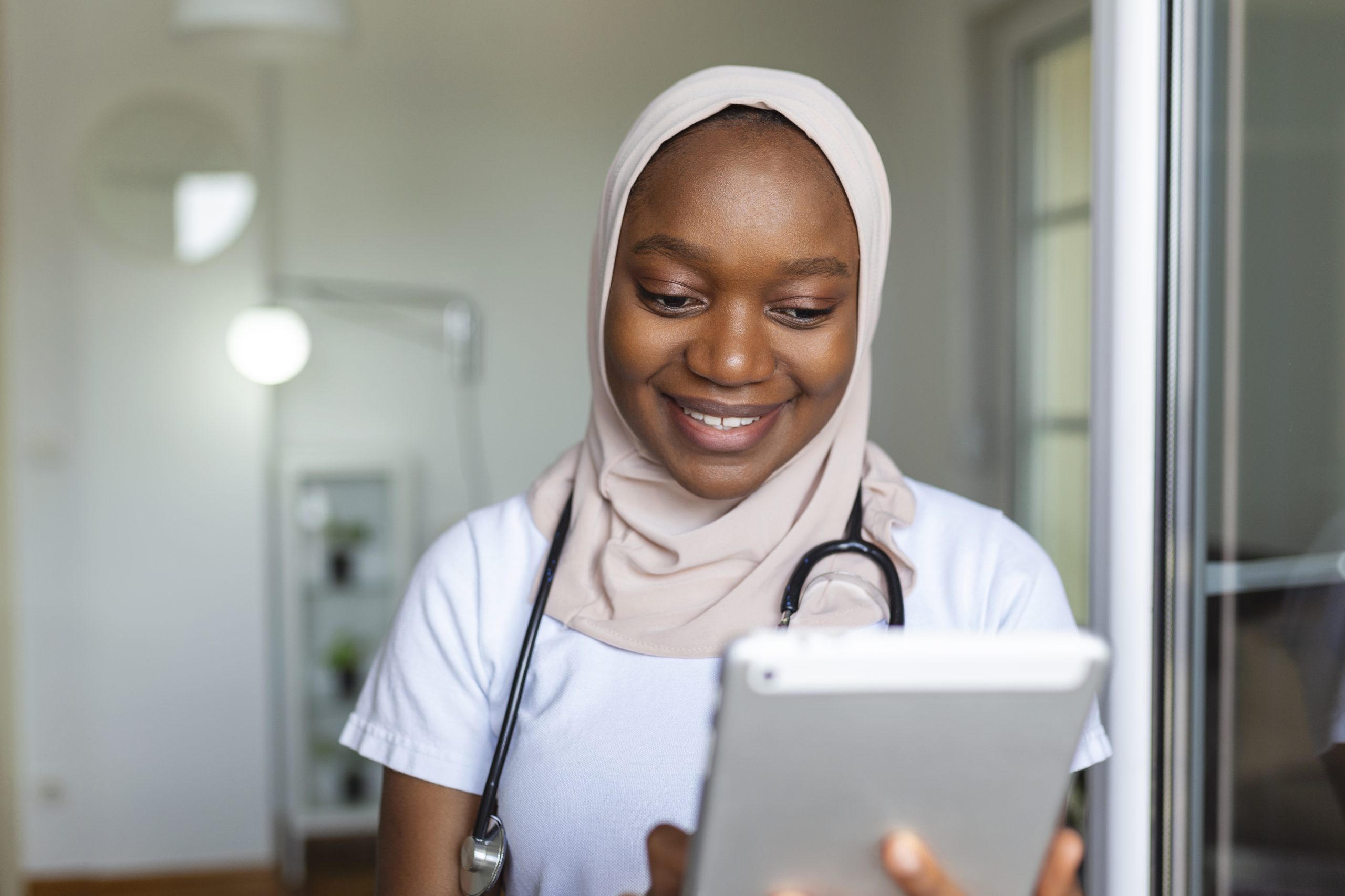 Young female musllim African clinician doctor in scrubs using touchpad while communicating with patients online