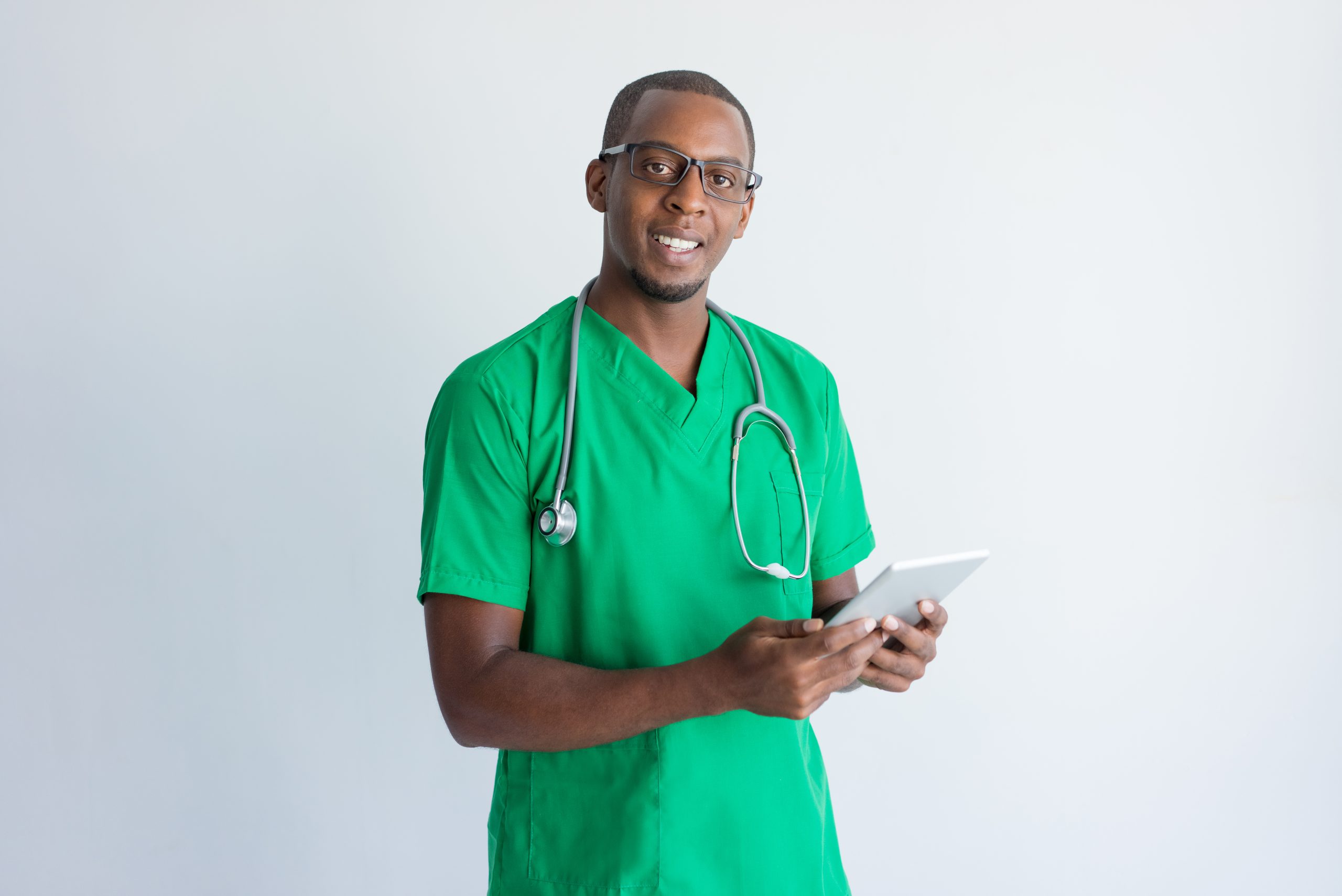 Portrait of happy general practitioner with digital tablet. Young African American medical student wearing glasses and green scrubs, looking at camera and smiling. Modern technology in medicine